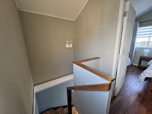 A room with a staircase, a wooden floor, a white wall, and a window with curtains.