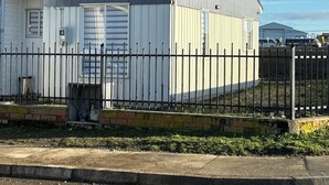 Un bâtiment à deux étages, à l’extérieur gris, avec une fenêtre blanche et une clôture en métal noir.