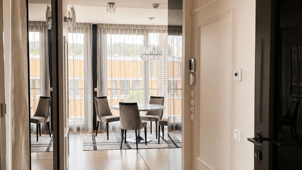 Een hotelkamer met een houten vloer, een zithoek met een ronde tafel en stoelen, en een groot raam met gordijnen.