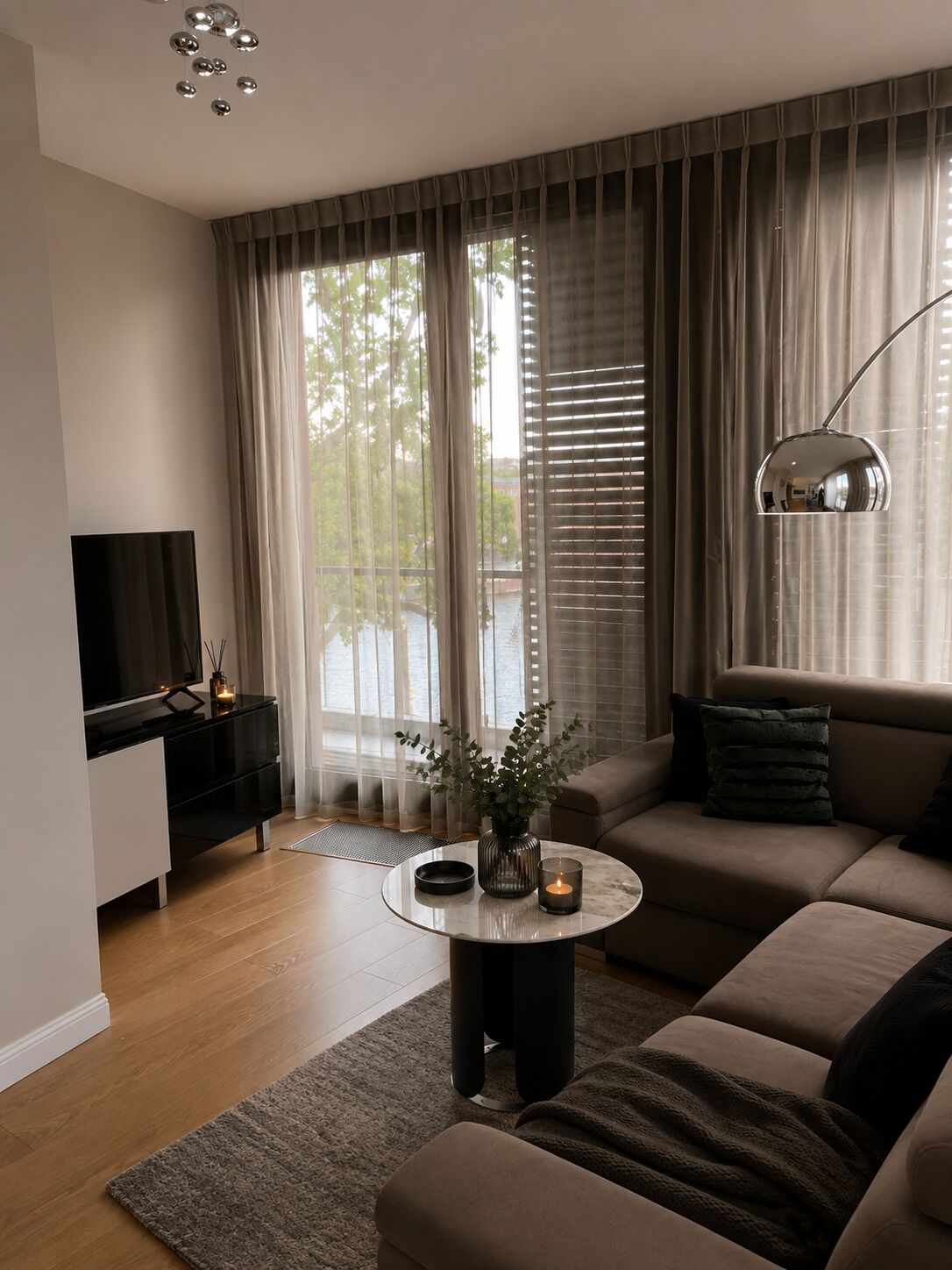 A modern living room with a sofa, a coffee table, a TV, and a large window with curtains.