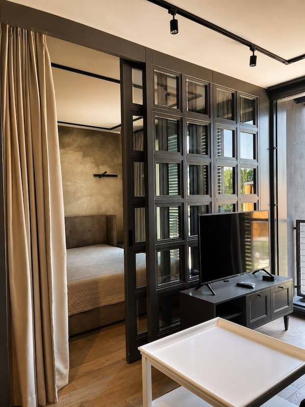 A modern bedroom with a bed, a desk, and a large window with blinds.