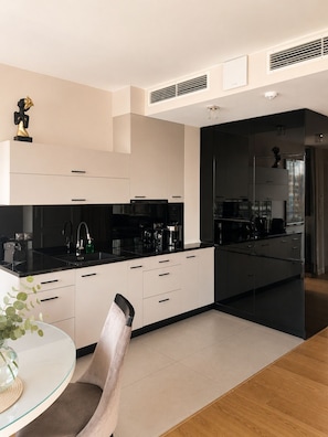 A modern kitchen with black countertops, white cabinets, and a glass dining table with a chair.