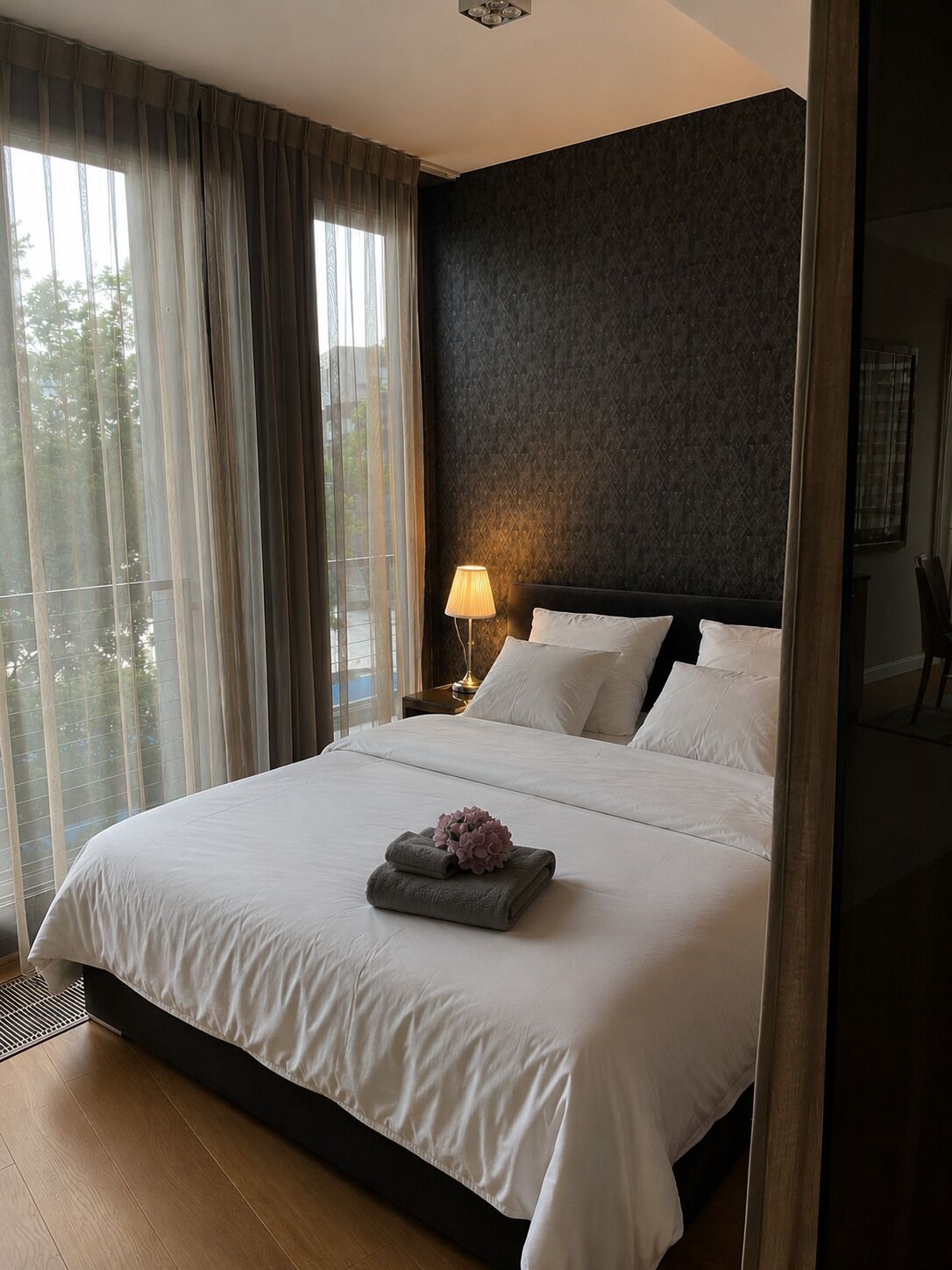 Ein Hotelzimmer mit einem großen Bett, einer Nachttischlampe und Blick aus dem Fenster.
