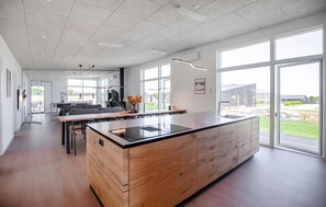 A modern kitchen with a large island, a dining area with a sofa, and large windows offering a view of the outdoors. - Gorgeous home in Børkop with sauna (Børkop)