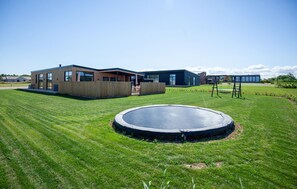 A modern building with a flat roof, a grassy lawn, and a trampoline in the foreground. - Gorgeous home in Børkop with sauna (Børkop)