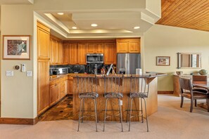 A modern kitchen with wooden cabinets, stainless steel appliances, and a central island with bar stools. - Storm Meadows Retreat | Pool & Hot Tub | Pet Friendly (Steamboat Springs)
