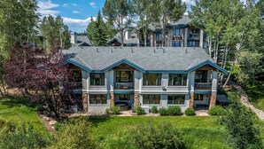 A multi-story house with a large front lawn, a covered patio, and a stone foundation. - Storm Meadows Retreat | Pool & Hot Tub | Pet Friendly (Steamboat Springs)