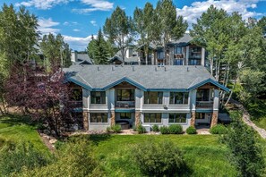A multi-story house with a large front lawn, a covered patio, and a stone foundation. - Storm Meadows Retreat | Pool & Hot Tub | Pet Friendly (Steamboat Springs)