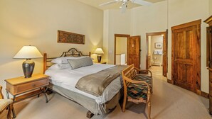 A hotel room with a bed, bedside lamps, a wooden chair, a ceiling fan, and a door leading to another room. - Storm Meadows Retreat | Pool & Hot Tub | Pet Friendly (Steamboat Springs)