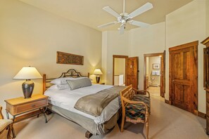 A hotel room with a bed, bedside lamps, a wooden chair, a ceiling fan, and a door leading to another room. - Storm Meadows Retreat | Pool & Hot Tub | Pet Friendly (Steamboat Springs)