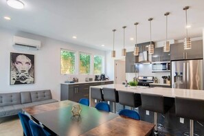 A modern kitchen with stainless steel appliances, a dining area with a dark wooden table, and a gray sofa. - 6BR Hot Tub | 5 Min to DT | Large Groups Unit A (Austin)
