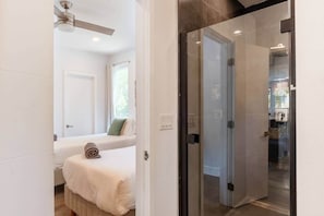 A hotel room with a bed, a window, a ceiling fan, and a glass door leading to a bathroom. - 6BR Hot Tub | 5 Min to DT | Large Groups Unit A (Austin)