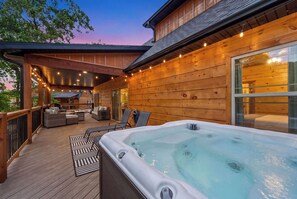 A wooden deck with a hot tub, outdoor seating, and string lights. - 3BR Cabin, Sleeps 8, Fire Pit + Hot Tub (Hollister)