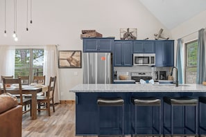 A modern kitchen with a central island, stainless steel appliances, and a dining area with wooden furniture. - 3BR Cabin, Sleeps 8, Fire Pit + Hot Tub (Hollister)