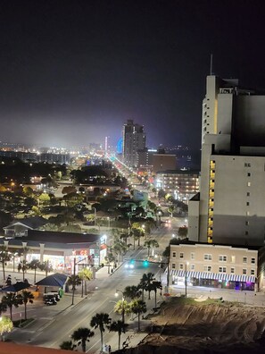 Paisagem urbana noturna com edifícios iluminados, uma roda gigante em destaque e uma rua com palmeiras.