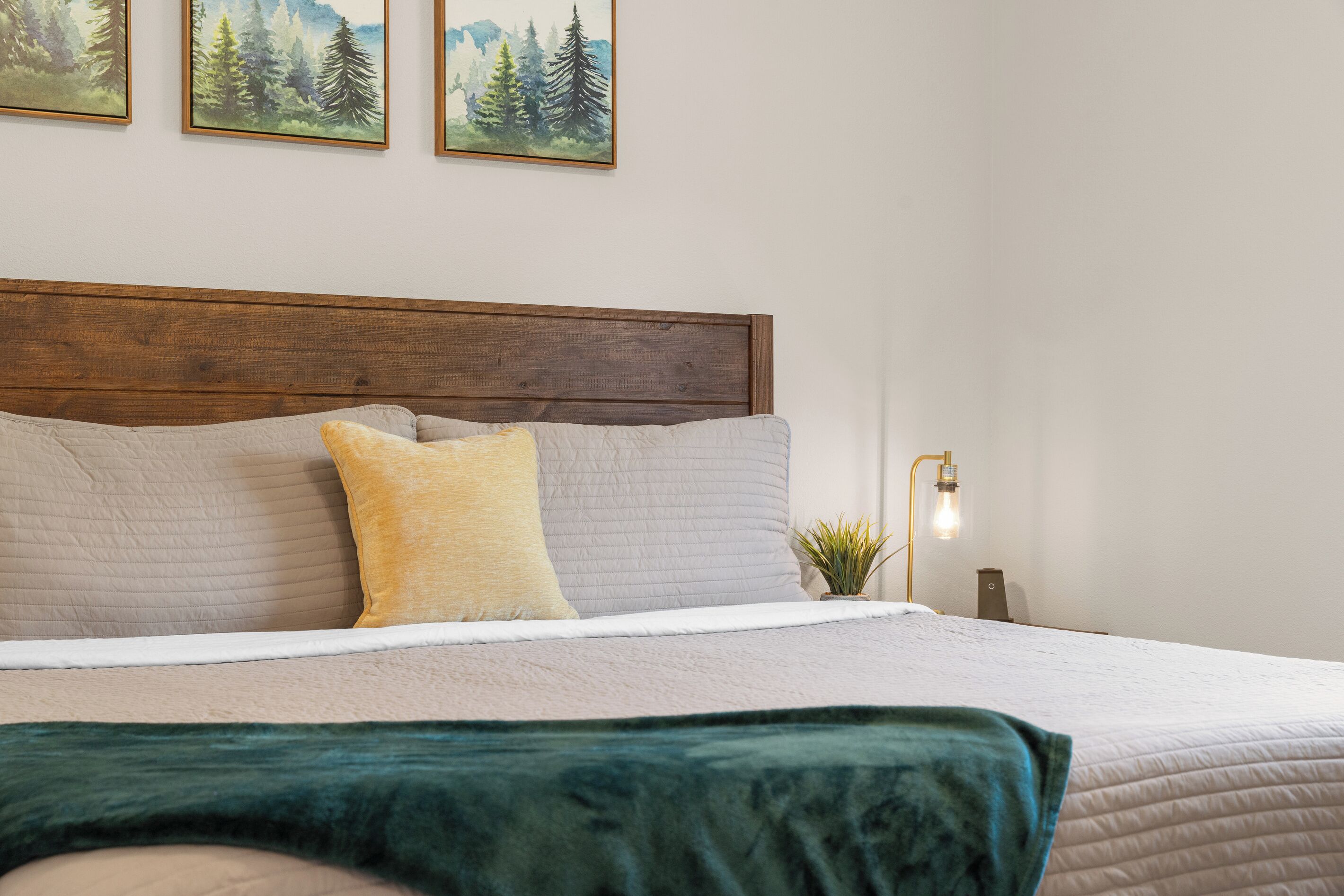 A bed with a wooden headboard, multiple pillows, a green blanket, and a wall-mounted lamp.