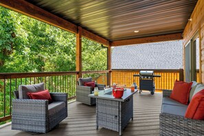 Eine überdachte Terrasse im Freien mit Korbmöbeln, einem Grill und Blick auf ein bewaldetes Gebiet.