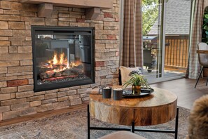 Una sala de estar moderna con una chimenea de piedra, una mesa de centro redonda de madera y un puerta de vidrio que da al exterior.