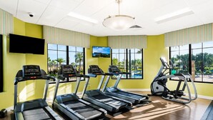 A gym with treadmills, an elliptical, and a stationary bike, large windows with a view of palm trees, and a flat-screen TV on the wall. - Resort Style 4-bedroom townhome - Close to Disney (Kissimmee)