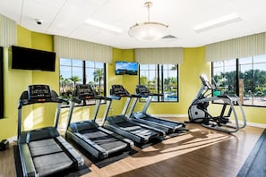 A gym with treadmills, an elliptical, and a stationary bike, large windows with a view of palm trees, and a flat-screen TV on the wall. - Resort Style 4-bedroom townhome - Close to Disney (Kissimmee)