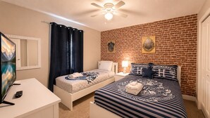 A bedroom with a brick wall, two beds, a ceiling fan, a TV, and a remote control. - Resort Style 4-bedroom townhome - Close to Disney (Kissimmee)