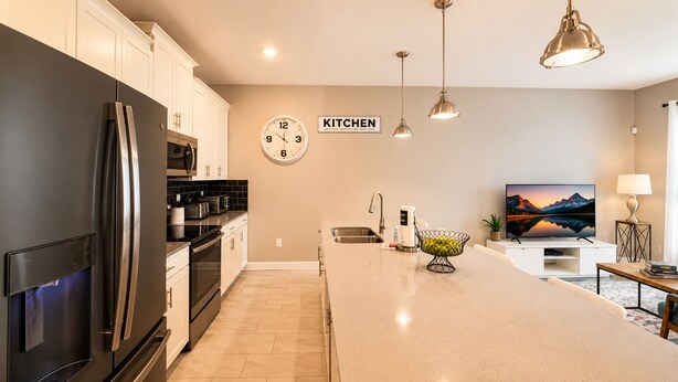 A modern kitchen with a large island, stainless steel appliances, and a clock on the wall. - Resort Style 4-bedroom townhome - Close to Disney (Kissimmee)