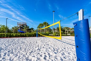 Un terrain de beach-volley avec un filet, des palmiers et un toboggan aquatique en arrière-plan.