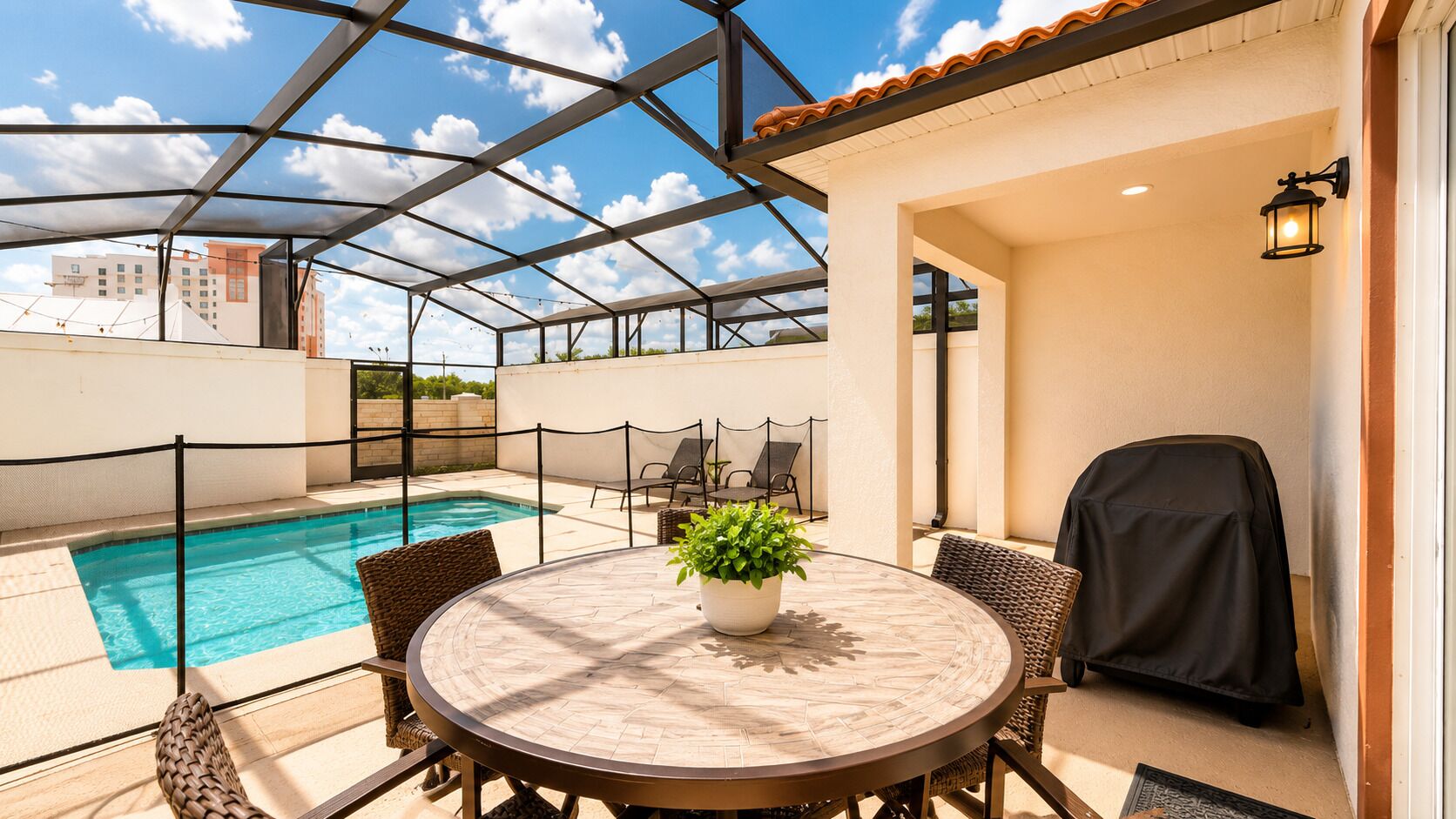 A covered outdoor area with a pool, a round table with chairs, and a potted plant.