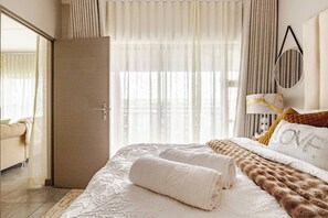 Ein Hotelzimmer mit Bett, Nachttisch, Lampe und Blick ins Freie.