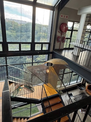 A multi-level interior with a spiral staircase, large windows offering a view of the outdoors, and a fire extinguisher mounted on the wall. - Waterfall Executive Suite (Johannesburg)