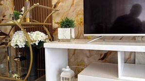 Ein modernes Wohnzimmer mit Flachbildfernseher, einer goldfarbenen Lampe, einer weißen Unterhaltungseinheit und einer Wand mit Marmoroptik.