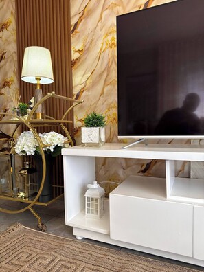 Ein modernes Wohnzimmer mit Flachbildfernseher, einer goldfarbenen Lampe, einer weißen Unterhaltungseinheit und einer Wand mit Marmoroptik.