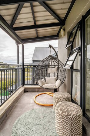 Ein Balkon mit einer Hängematte, einem Hocker und Blick auf die Landschaft.