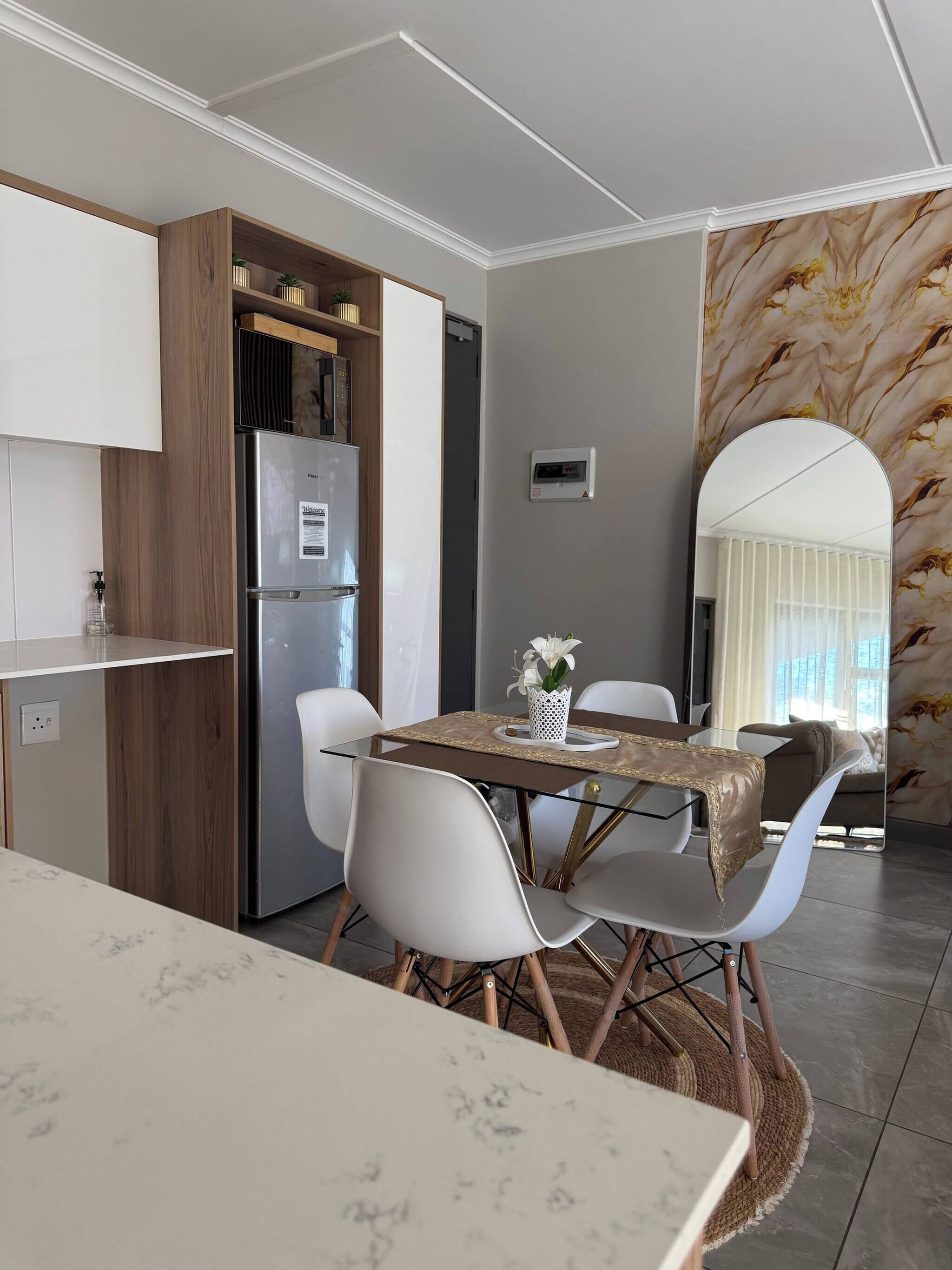 A modern kitchen with a built-in refrigerator, wooden cabinets, and a dining area with a glass table and white chairs.