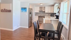 Una cucina moderna con elettrodomestici in acciaio inossidabile, una zona pranzo con tavolo e sedie e vista sull'esterno attraverso una finestra.