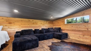 A room with a sectional sofa, wooden walls, a window, and a ceiling with a corrugated metal design. - Everything, In Montana, All At Once (Saint Regis)