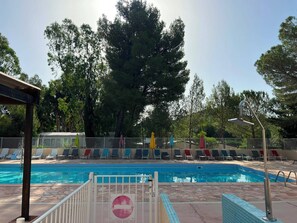 Ein Schwimmbecken mit einem Verbotsschild, umgeben von Liegestühlen und einem Zaun.