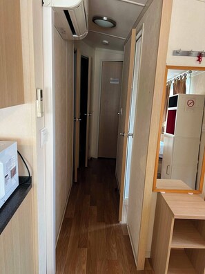 A narrow hallway with wooden flooring, a ceiling-mounted air conditioner, a door with a 'Chambre' sign, and a mirror reflecting a wardrobe and a red curtain. - Air-conditioned mobile home at a 4-star campground for 6–8 people, with a pool, 5 minutes from the beaches (La Londe-les-Maures)