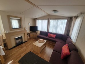 Ein Wohnzimmer mit einer Couch, einem Fernseher, einem Kamin und einem Fenster mit Vorhängen.