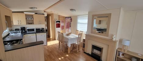 A compact kitchen with a dining area, wooden flooring, and a fireplace.