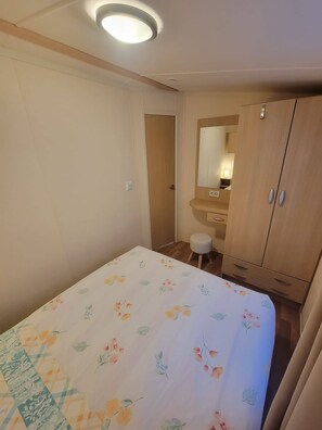 Ein Schlafzimmer mit einem Bett, einem kleinen Hocker, einem Schminktisch mit Spiegel und einem Kleiderschrank.