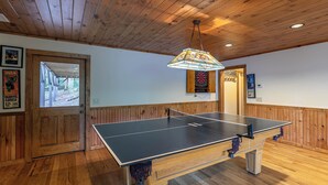 Et bordtennisbord i et rum med trævægge og -loft, en dør der fører udendørs, og en dartskive på væggen.