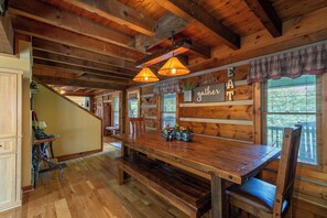 Ein rustikales Holzinterieur mit einem großen Holzesstisch, Bänken und einer Treppe, die in einen anderen Raum führt.