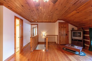 A wooden-floored hallway with a staircase, a television, and a small table. - Caris Rivers Edge Cabin - game room, Twin Rivers mountain home in Boone, fire pit (Boone)