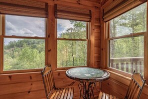A wooden cabin interior with large windows, a round table, and two chairs. - Lions Den- hot tub, pet friendly, 15 mins to Boone! (Vilas)