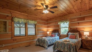 Ein Schlafzimmer in einer Blockhütte mit zwei Betten, einem Deckenventilator und Fenstern mit Vorhängen.
