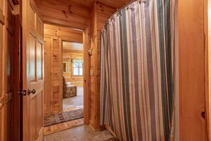 A wooden interior hallway with a striped curtain, a door, and a rug leading to a room with a window. - Lions Den- hot tub, pet friendly, 15 mins to Boone! (Vilas)