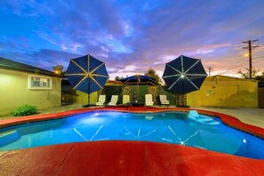 A swimming pool with two umbrellas, surrounded by lounge chairs and a red deck.