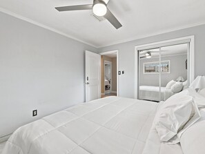 Ein Schlafzimmer mit Bett, Deckenventilator und einer Tür zu einem anderen Raum.