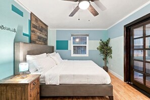 Ein Schlafzimmer mit Bett, Nachttisch, Lampe, Fenster und Deckenventilator.